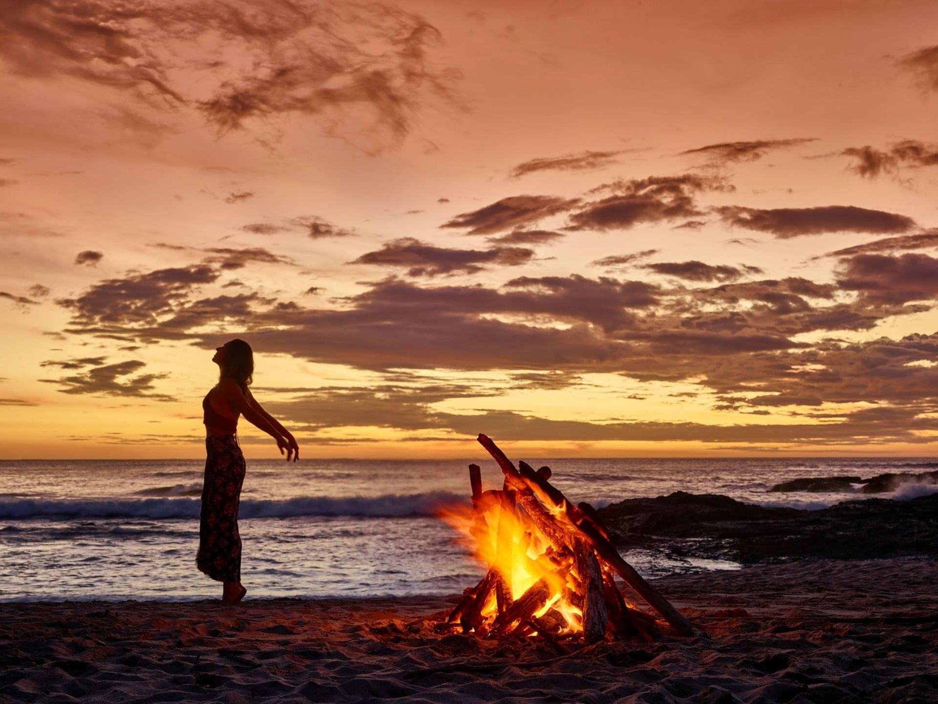 Peaceful sunset bonfire near with a woman silhouetted against the crashing waves Cala Luna Boutique Hotel