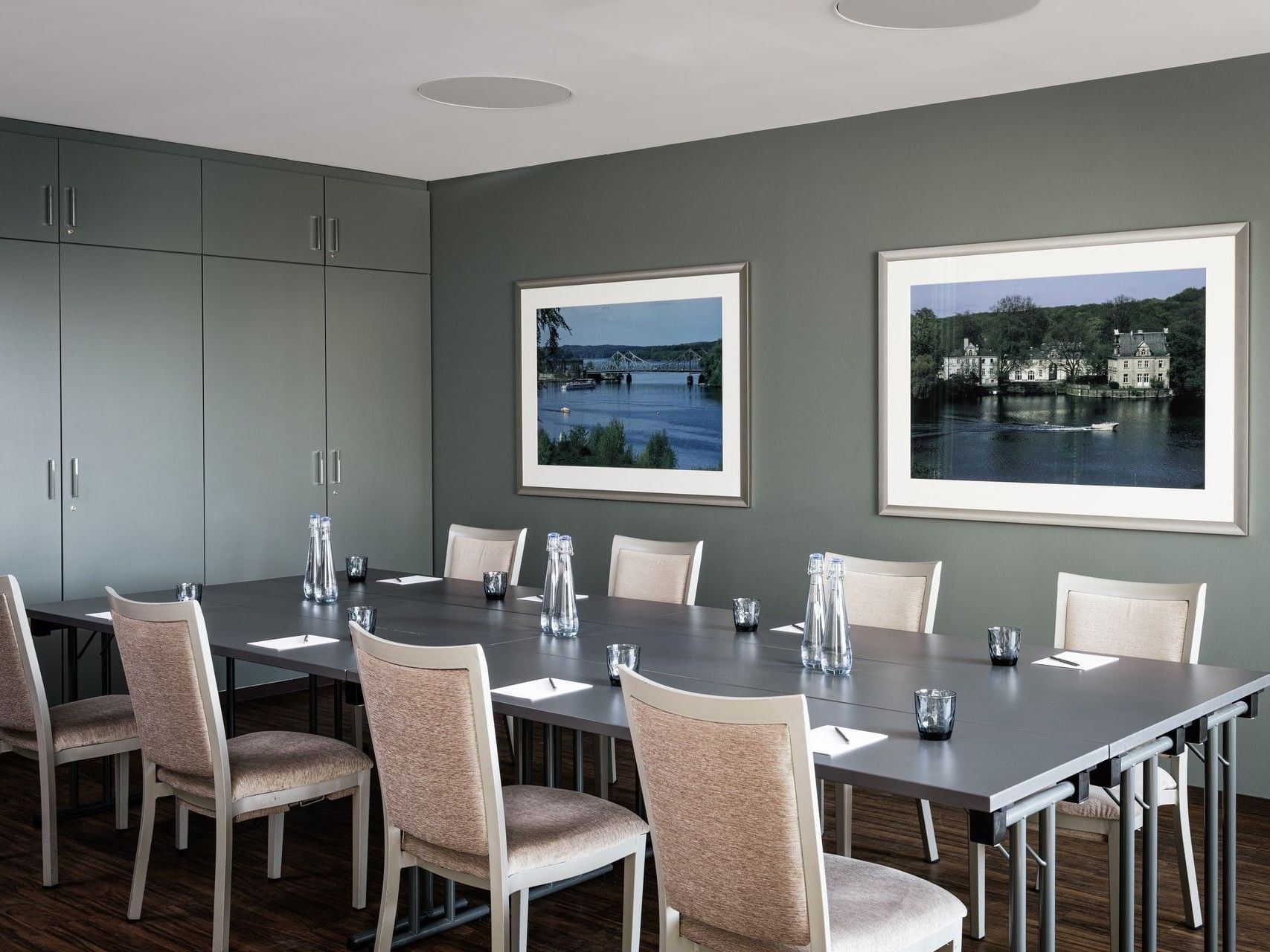 Ein langer Konferenztisch mit Stühlen, Wasserkrügen und gerahmten Landschaftsbildern an grünen Wänden.