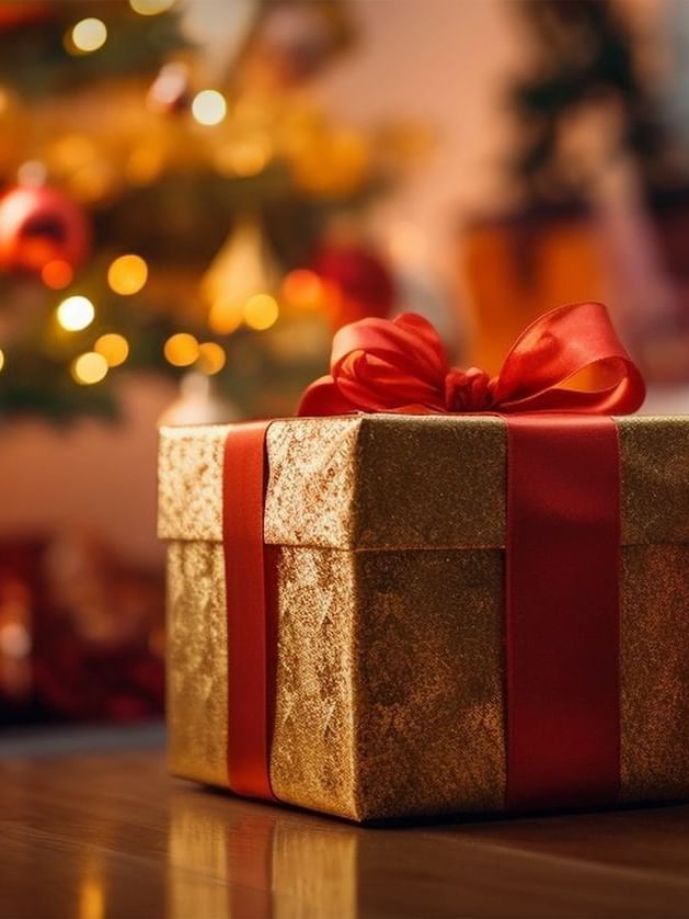 Gold gift box with a red ribbon placed by a glowing Christmas tree at Warwick Hotels & Resorts