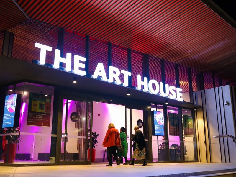 Illuminated THE ART HOUSE sign above the entrance with people, near Mercure Kooindah Waters