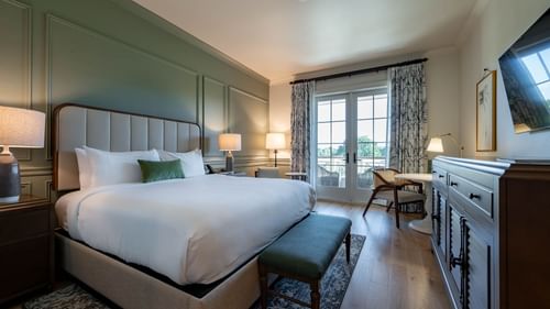 King bed with a cushioned headboard & wooden floors in Driving Range View King Room With Balcony at Camp Creek Inn