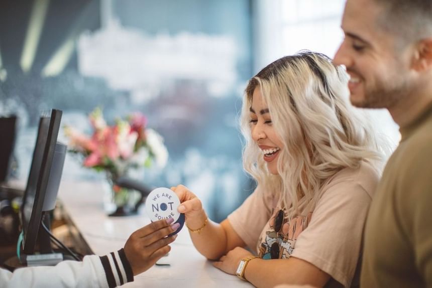 Guest smiling during check-in while receiving a We Are Not Square sticker at Hotel Angeleno, Los Angeles hotel boutique