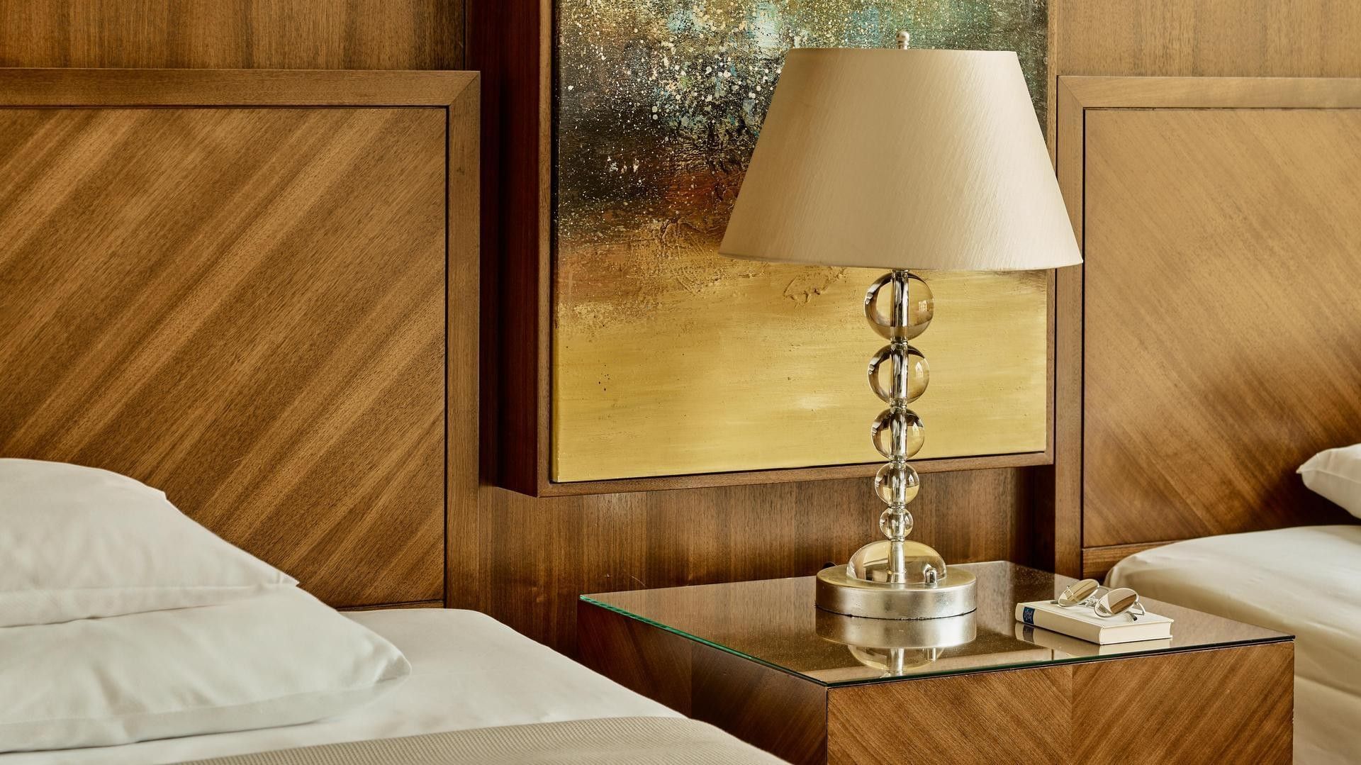 Elegantes Hotelzimmer mit zwei Betten, einer Lampe auf einem Glastisch und einem Gemälde an der Wand.