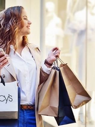 Woman holding shopping bags by a smartphone near Warwick San Francisco