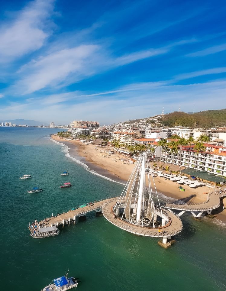 Aerial view of Los Muertos Pier with a white sail-like structure over the turquoise ocean coastline at Los Arcos Suites