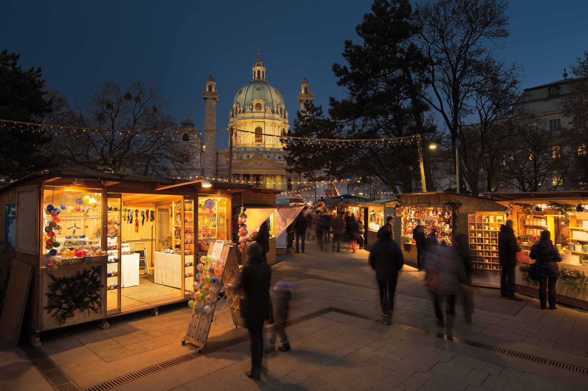 Advent market in front of Karlskirche in Vienna at dusk with illuminated market stalls and a festive atmosphere