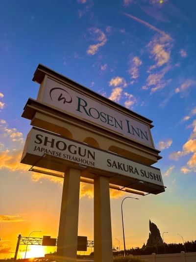 A sign reading Rosen Inn and Shogun Japanese Steakhouse Sakura Sushi silhouetted against a sunset sky.