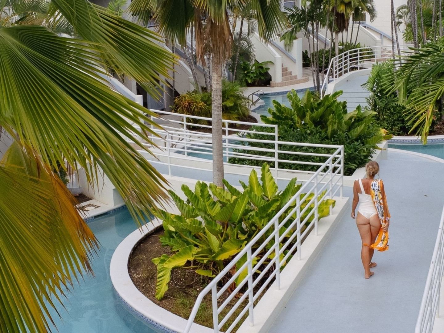A woman walks along a path with pool and tropical plants at Savannah Beach Hotel.