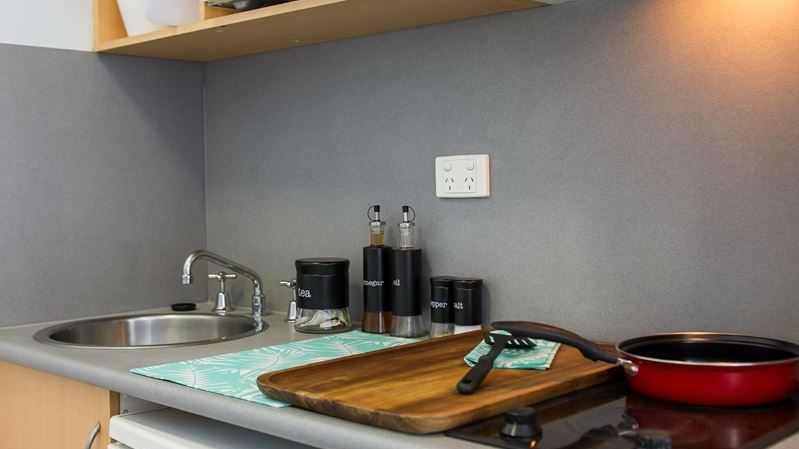 Compact kitchenette with microwave, stovetop, sink, and wooden shelving at StudentLiving - on Margaret