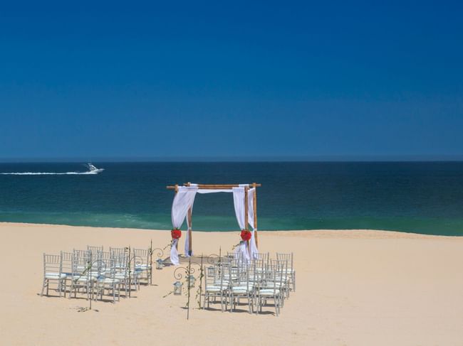 A stunning beach ceremony setup at Hacienda del Mar Los Cabos with a bamboo arch and white-draped chairs