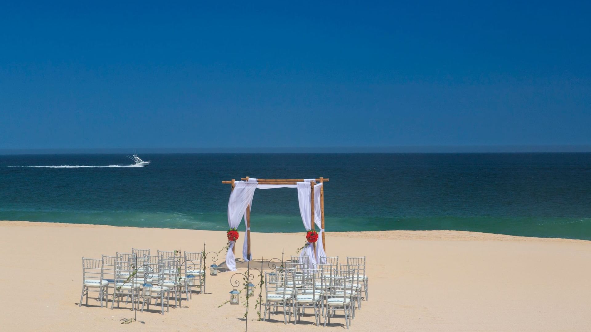 A stunning beach ceremony setup at Hacienda del Mar Los Cabos with a bamboo arch and white-draped chairs