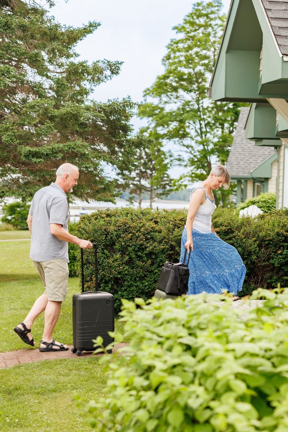 Couple with luggage walking by lush green bushes at Rodd Brudenell River Resort, one of the best accommodations in PEI