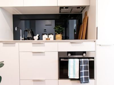 White kitchen with a black oven, towels, cabinets, sink, faucet, and a plant.