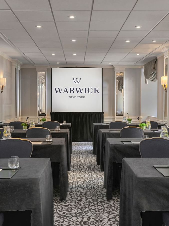 Sussex Meeting Room with black-covered tables, gray chairs, and water pitchers facing a screen at Warwick New York