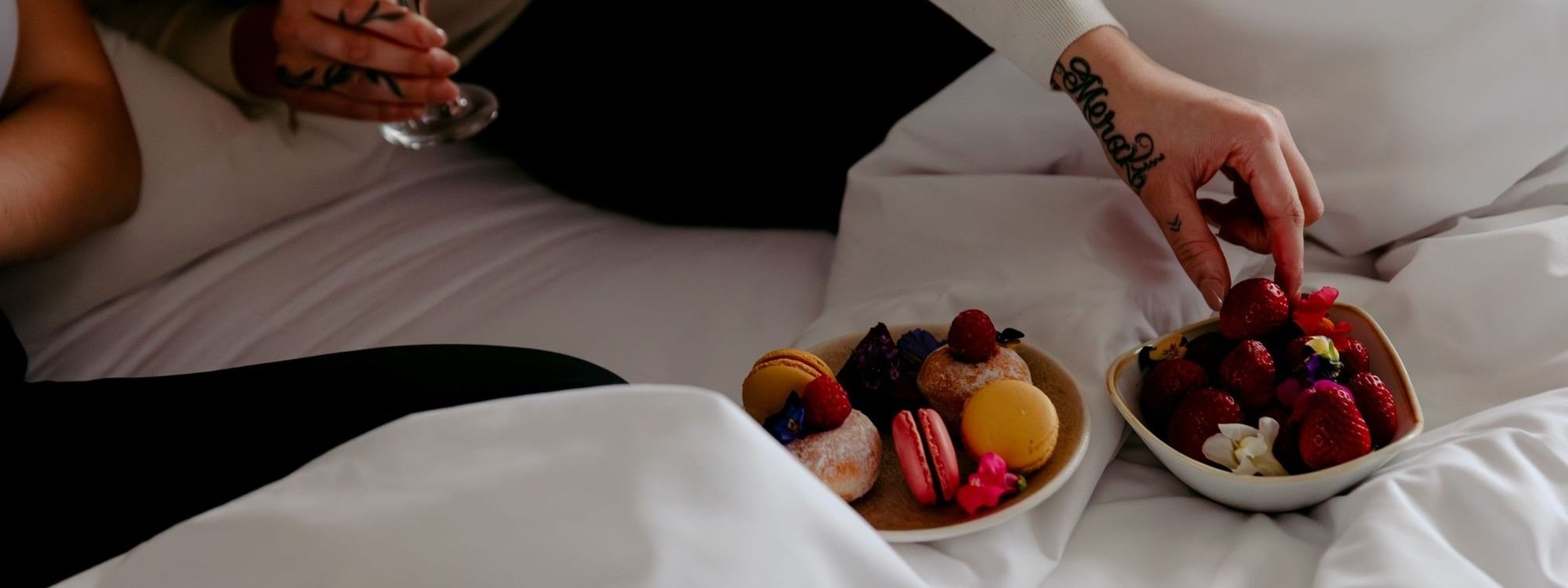 Couple enjoying desserts and champagne on bed, highlighting Novotel Sydney Parramatta dining experience