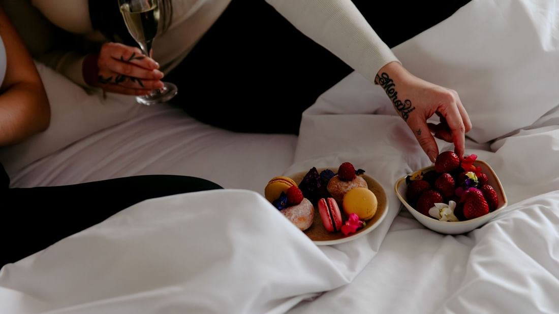 Couple enjoying desserts and champagne on bed, highlighting Novotel Sydney Parramatta dining experience.
