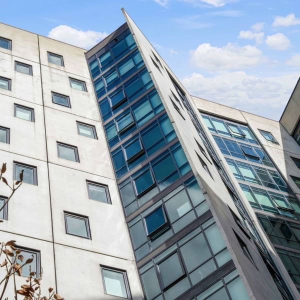 Modern glass and concrete building with many windows under a blue sky with clouds.