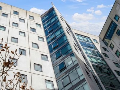 Modern glass and concrete building with many windows under a blue sky with clouds.