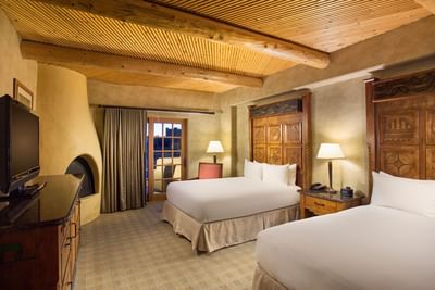 Cozy guest room at Hilton Santa Fe Buffalo Thunder with two beds, a fireplace, and a rustic wooden ceiling