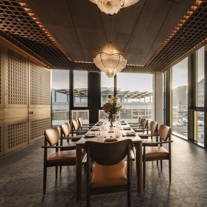 Sala da pranzo con tavolo lungo, sedie, centrotavola floreale, e grandi finestre con vista esterna.