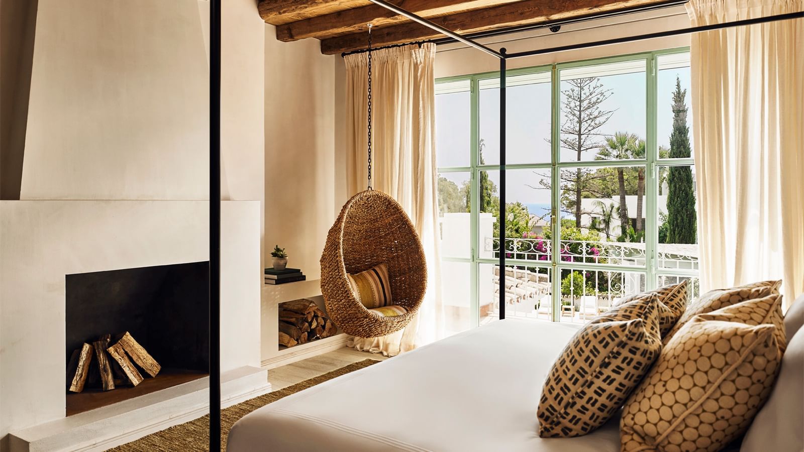 Room with a hanging rattan chair by a large window, opposite the bed at the Marbella Club