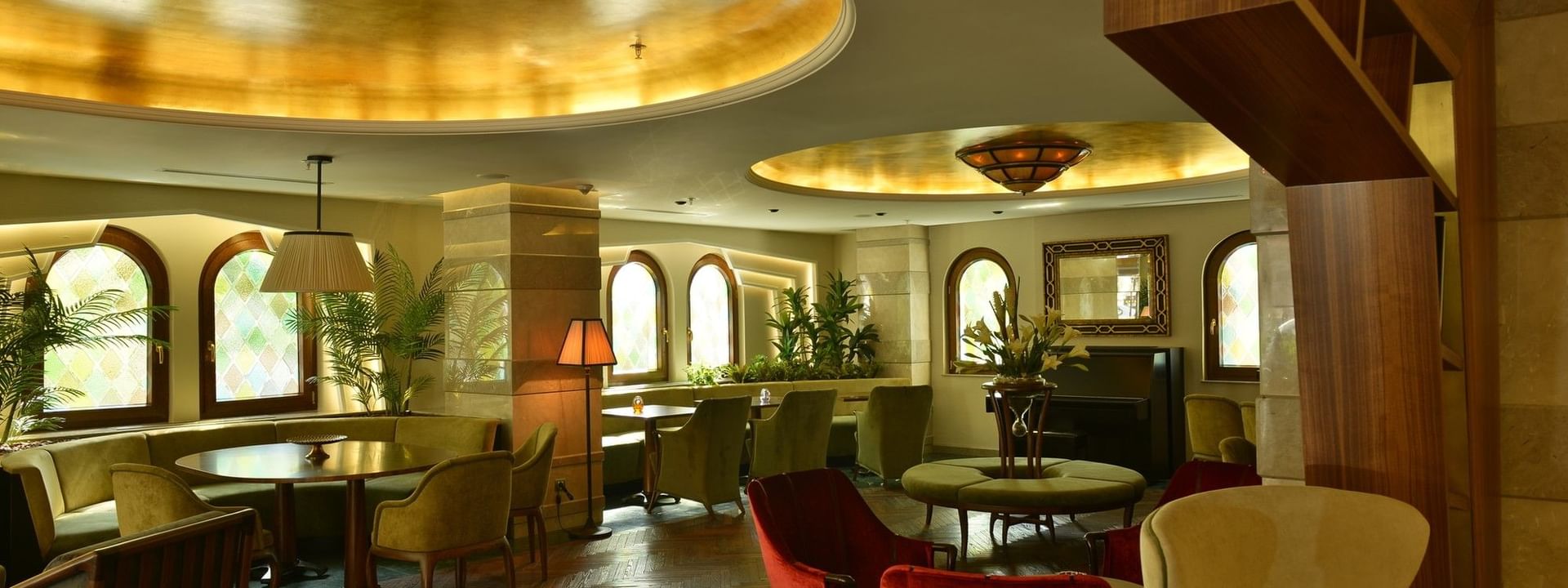Lobby Lounge with red velvet armchairs by green chairs under a warm gold ceiling at Warwick Ankara