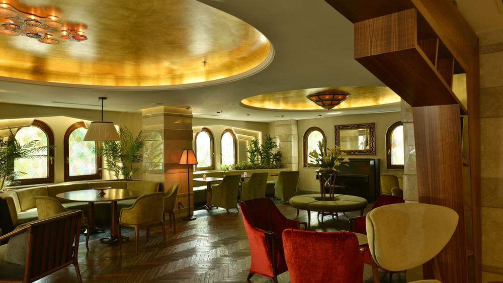Lobby Lounge with red velvet armchairs by green chairs under a warm gold ceiling at Warwick Ankara