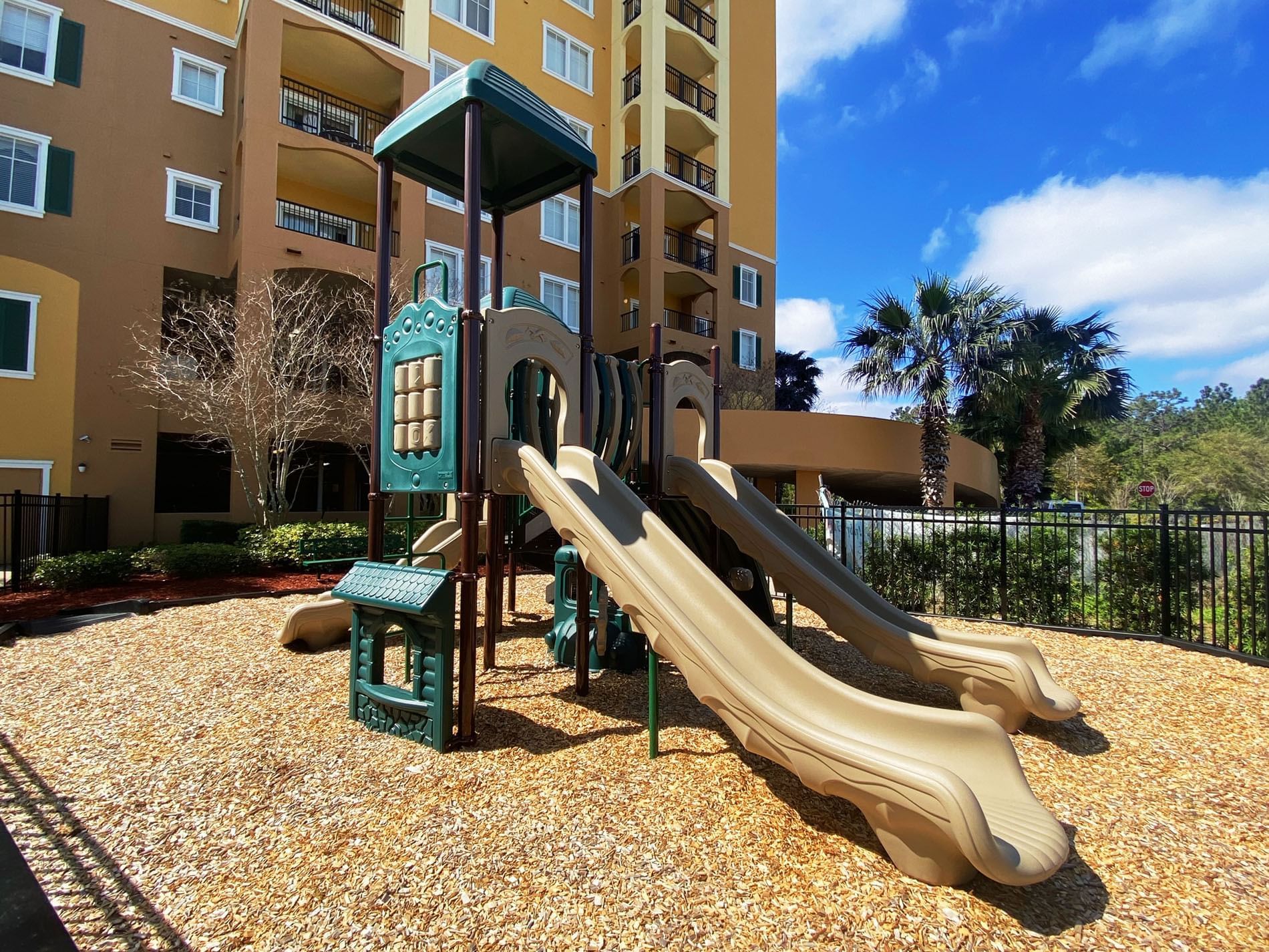 A playground with a climbing structure and slides in front of a multi-story building.