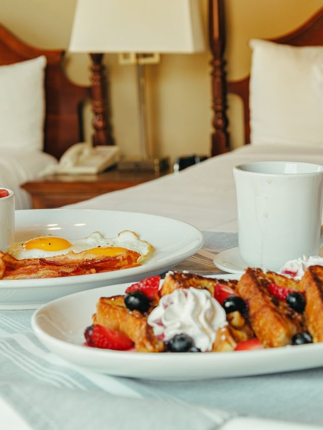 Plates of French toast and eggs by a coffee mug on a white bed at the Arlington Resort Hotel & Spa