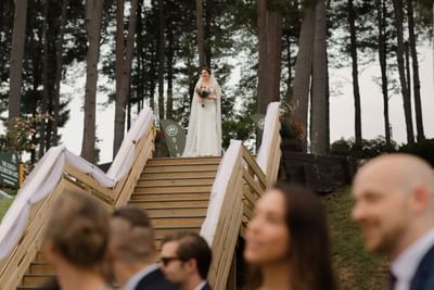 Bride standing at the top of staircase in a forest setting in The Lodge at Schroon Lake