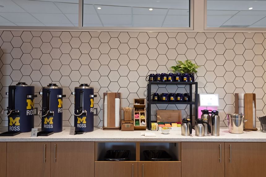 Michigan Ross Coffee station with three coffee dispensers, a shelf with cups, and a counter.