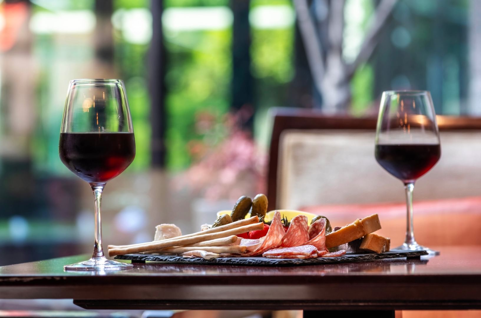 Two glasses of red wine are on a table with a charcuterie board  in The Lounge Bar & Terrace at Warwick Reine Astrid - Lyon