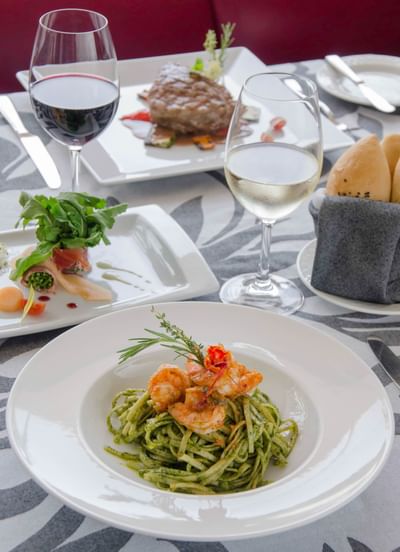 Tres platos gourmet, una copa de vino, una copa de agua y panera sobre la mesa de un restaurante del Sunset Plaza Beach Resort, uno de los mejores hoteles con vistas a la playa en Puerto Vallarta