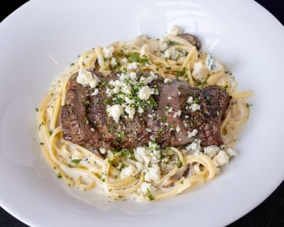 Fettuccine pasta topped with a grilled steak and crumbled cheese served at The Ashbrook Hotel