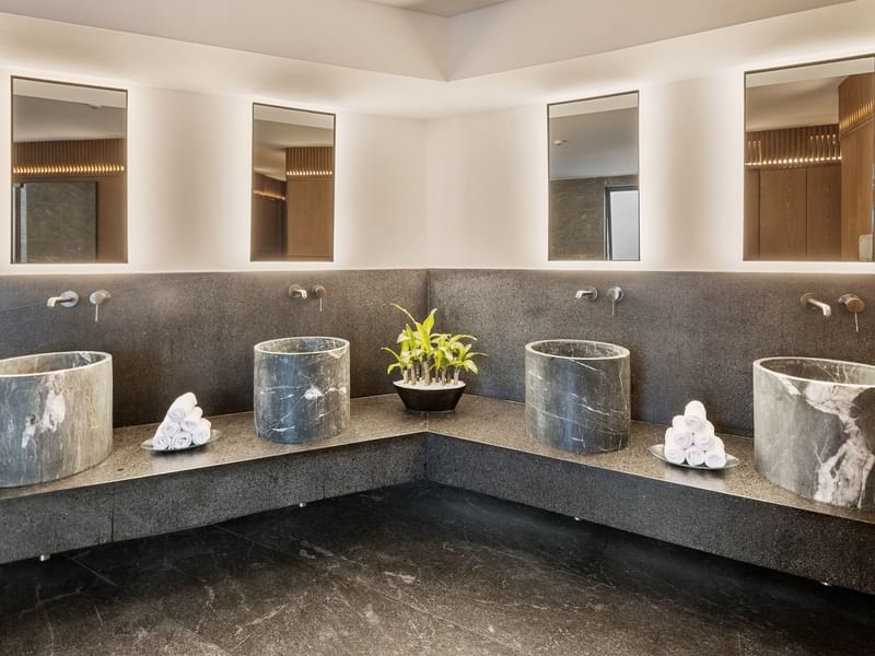 Modern bathroom with three marble basins, backlit mirrors, and a black counter at Grand Fiesta Americana