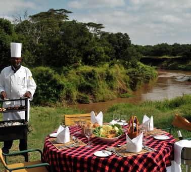 An outdoor dining area by the river at Sweetwaters Serena Camp