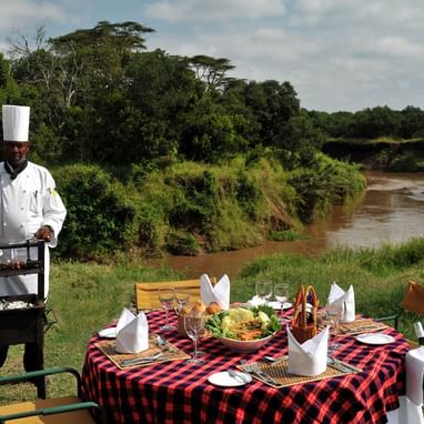 An outdoor dining area by the river at Sweetwaters Serena Camp