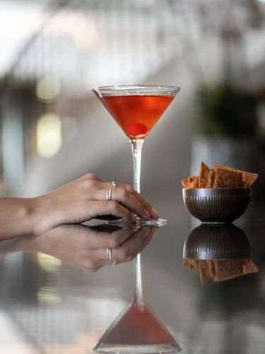 Une main tendue vers un cocktail au Téséo Bar de l'hôtel Warwick Geneva [BETA].