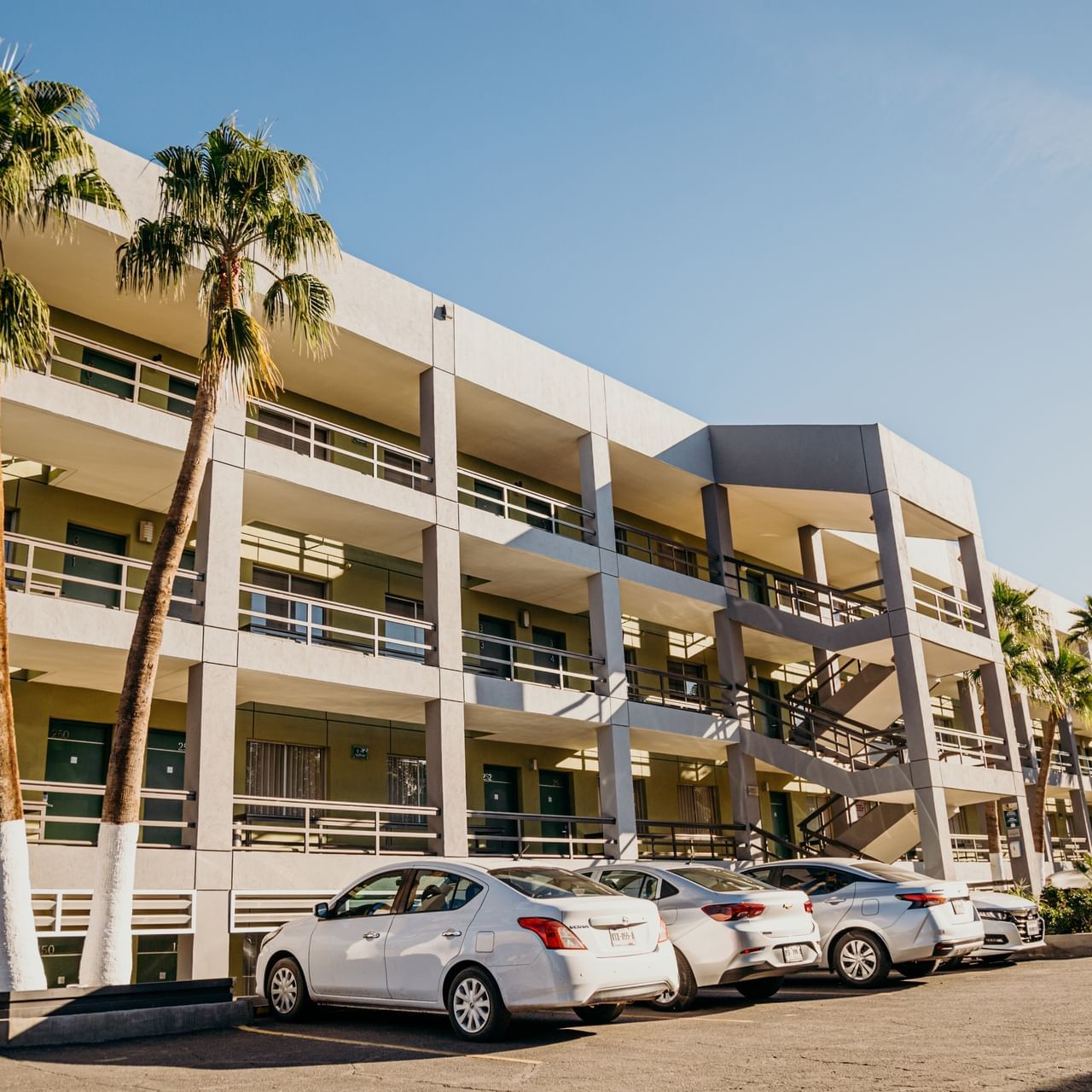 Edificio de varios pisos de Araiza Calafia, con coches en el estacionamiento, palmeras y escaleras exteriores en día soleado 