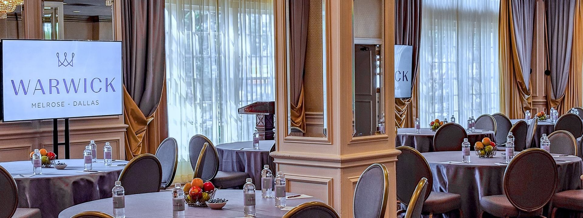 Event tables by a TV screen under crystal chandeliers in Crystal Ballroom at Warwick Melrose Dallas