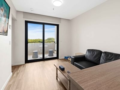 Black leather sofa, wooden table, and glass balcony in a modern hotel room.
