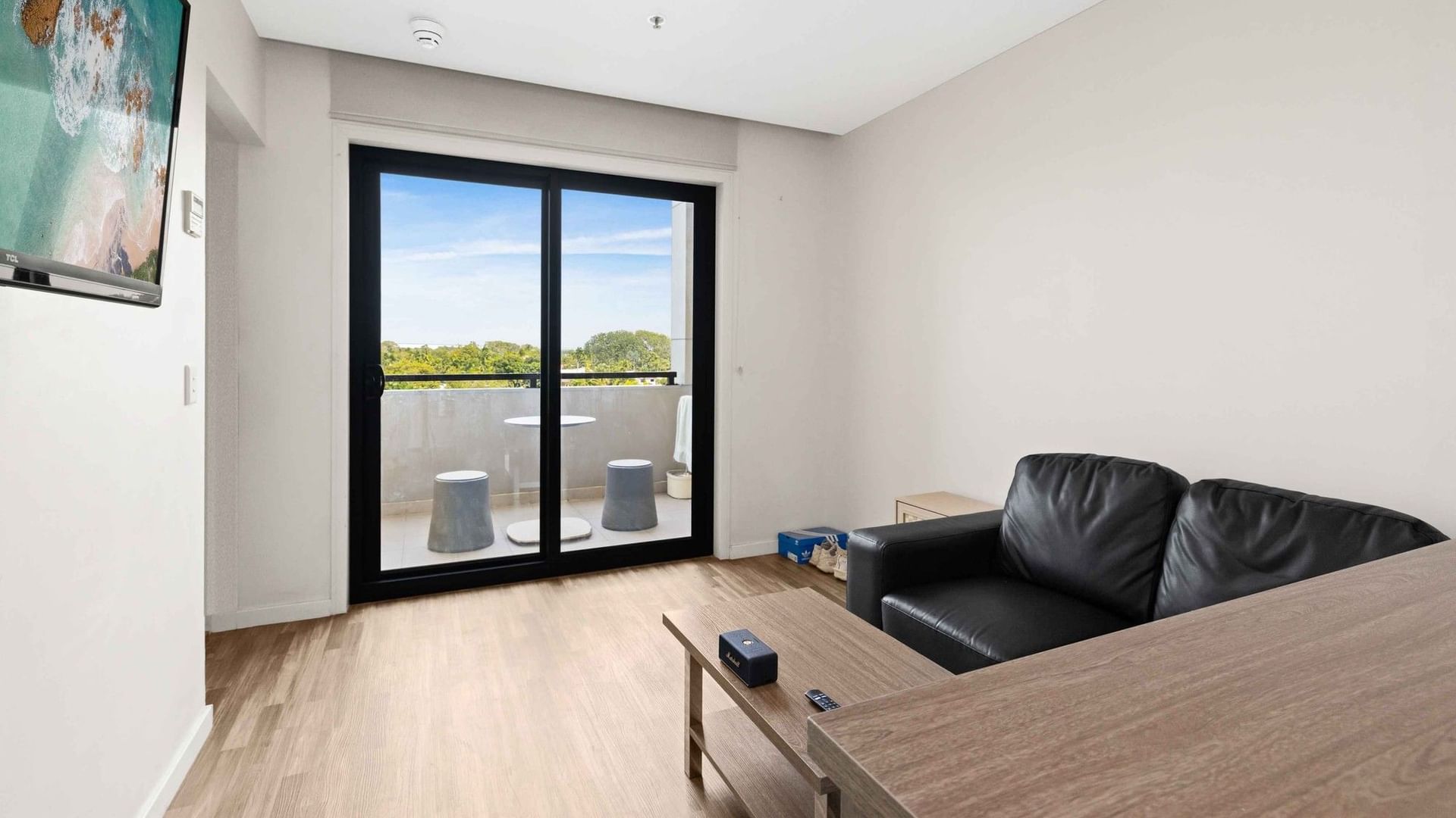 Black leather sofa, wooden table, and glass balcony in a modern hotel room.