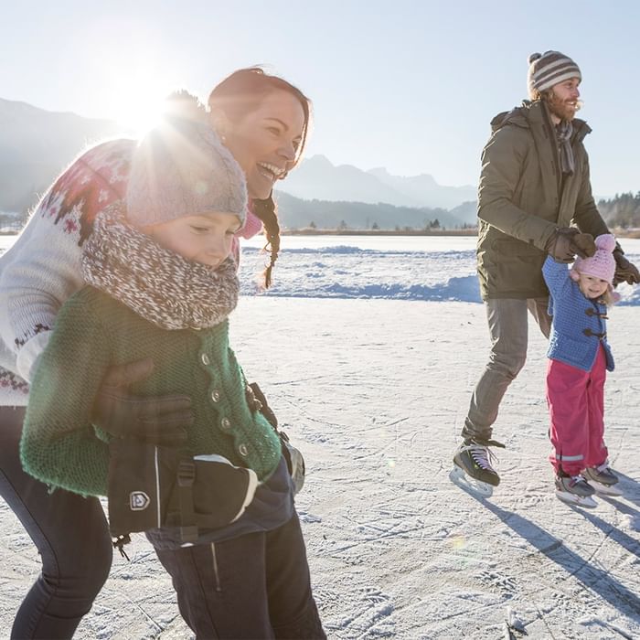 Famiglia felice pattinando sul ghiaccio con montagne innevate sullo sfondo at Falkensteiner Group