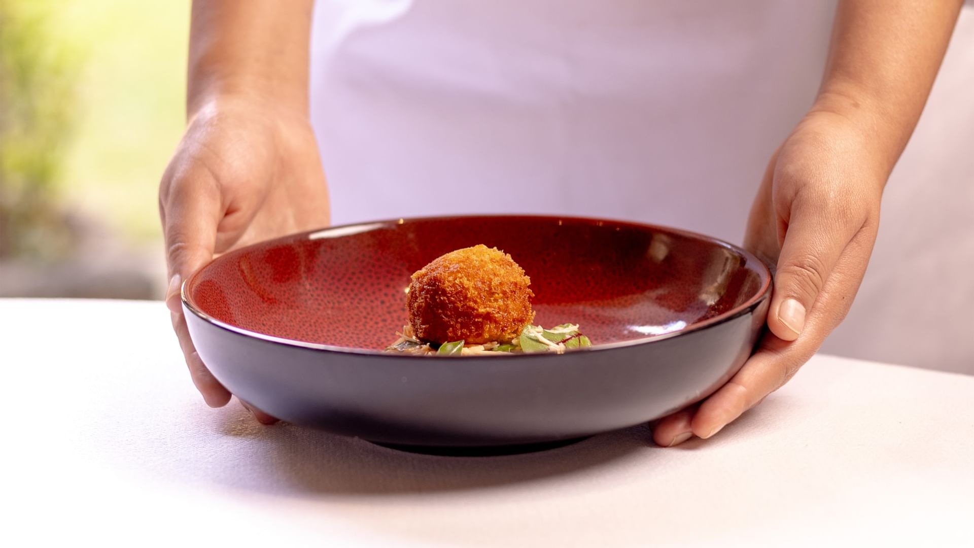 A hand holding a red bowl with a golden fried appetizer and green herbs at Quinta Real Oaxaca