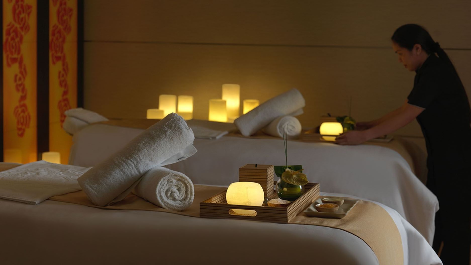 Woman preparing vanity in a spa room lit with candles at DAMAC Maison Cour Jardin