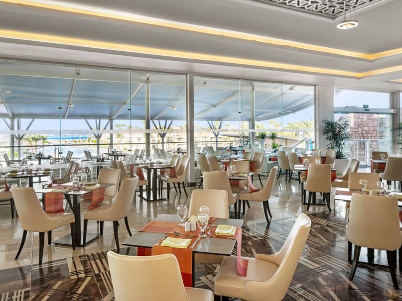 Elegant restaurant with beige chairs, glass walls, and tables set with wine glasses and napkins.