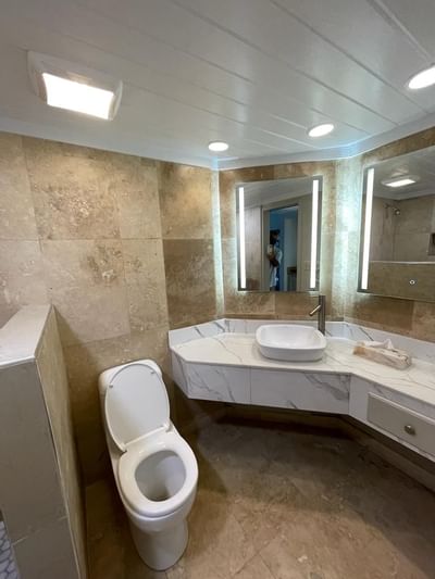 White marble vanity with vessel sink and illuminated mirrors next to the toilet in the bathroom at Emerald Beach Resort