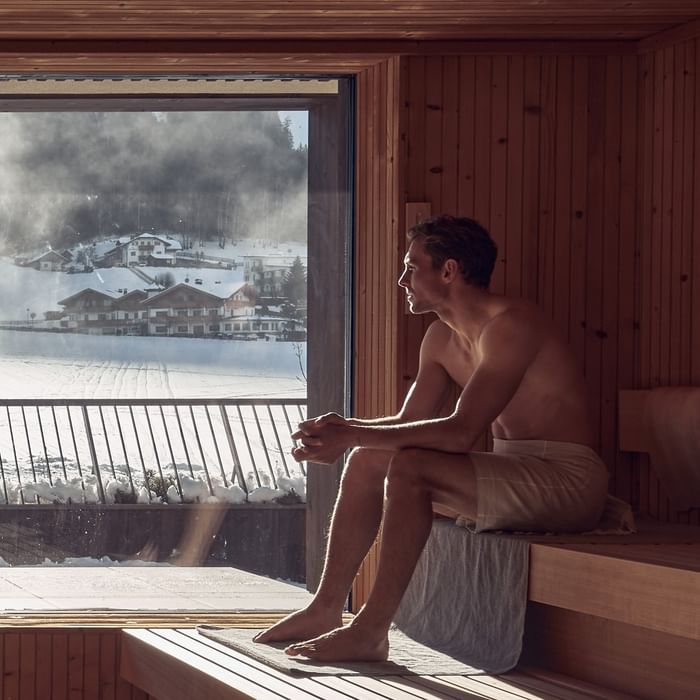 Uomo seduto in sauna con vista su paesaggio innevato del Falkensteiner Group