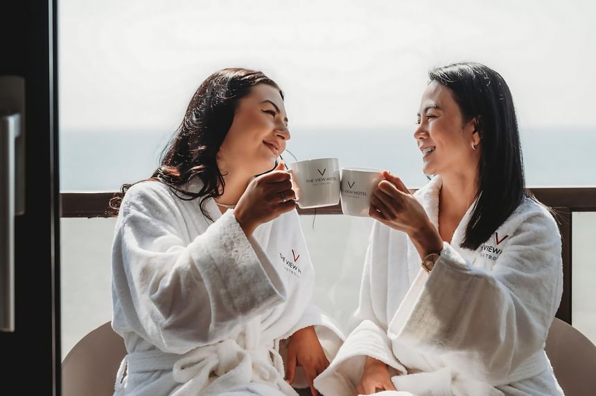 Two women in bathrobes with The View Hotel logo on them enjoying a cup of coffee at The View Hotel Eastbourne