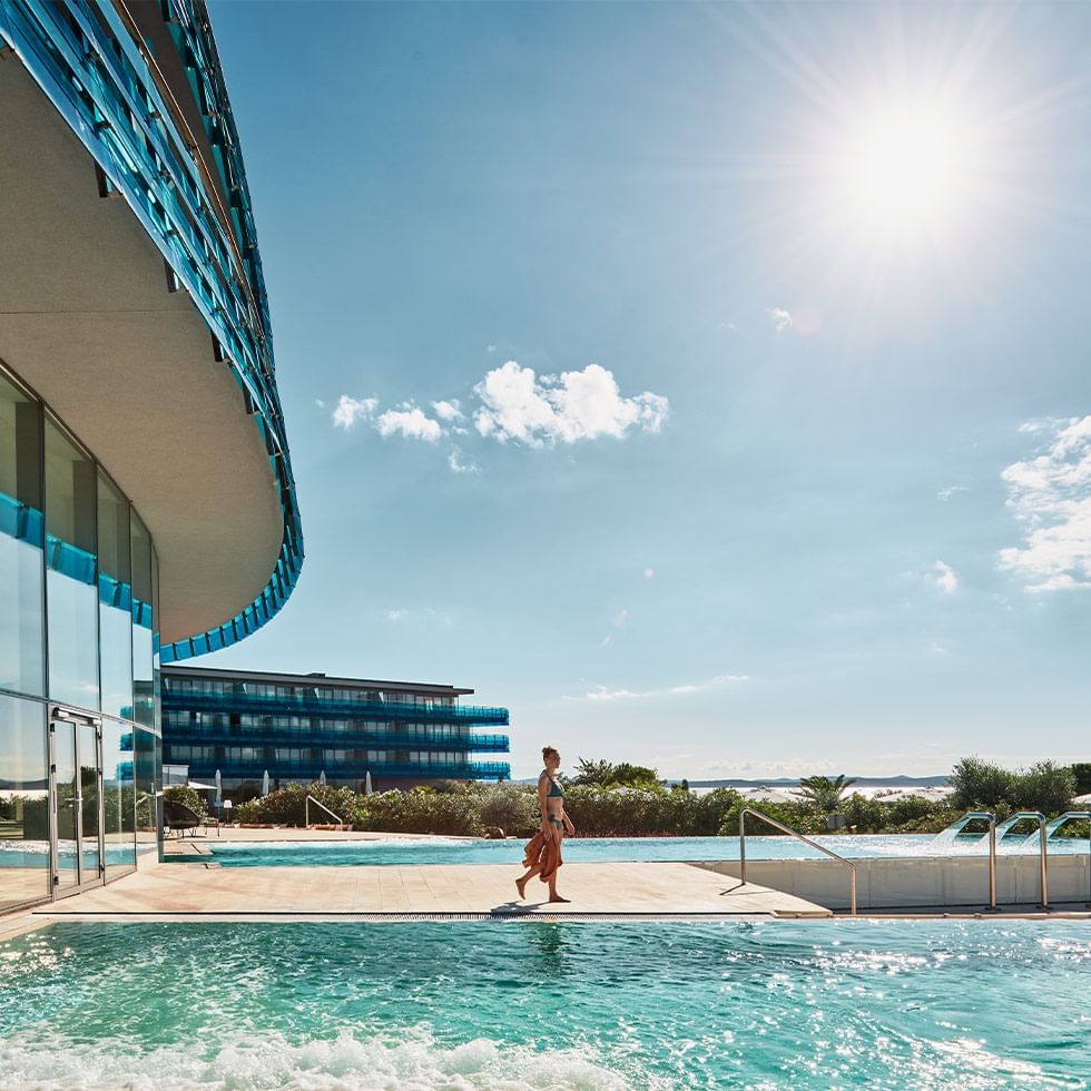 A woman walking towards the pool at Falkensteiner Hotels